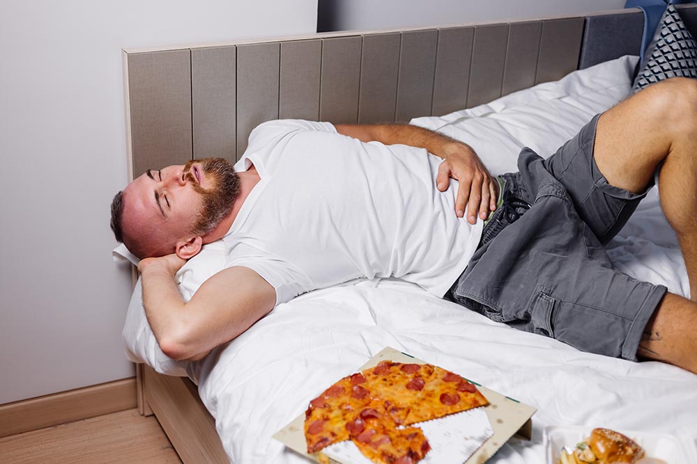 caucasian bearded man lies bad after overate fast food pizza burgers