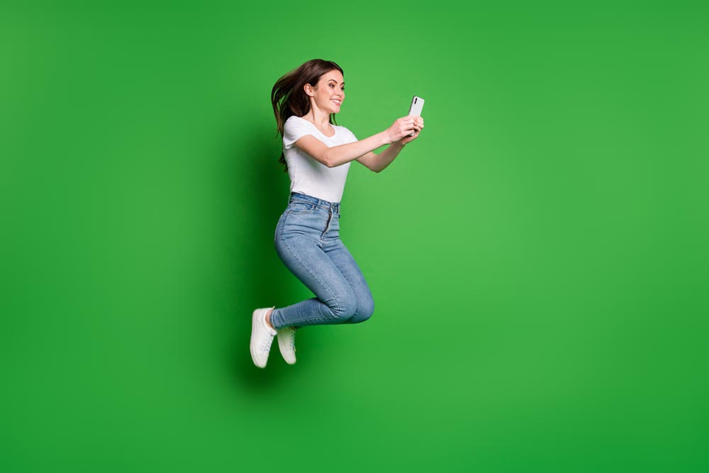 Full size photo of girl jump use smart phone wear white denim is